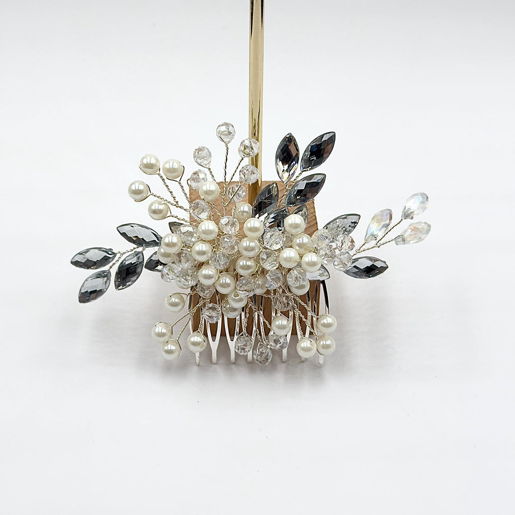 Bride in side profile wearing a floral bridal hair comb above a low bun, decorated with white pearls, clear crystals and sparkling leaf-shaped stones.