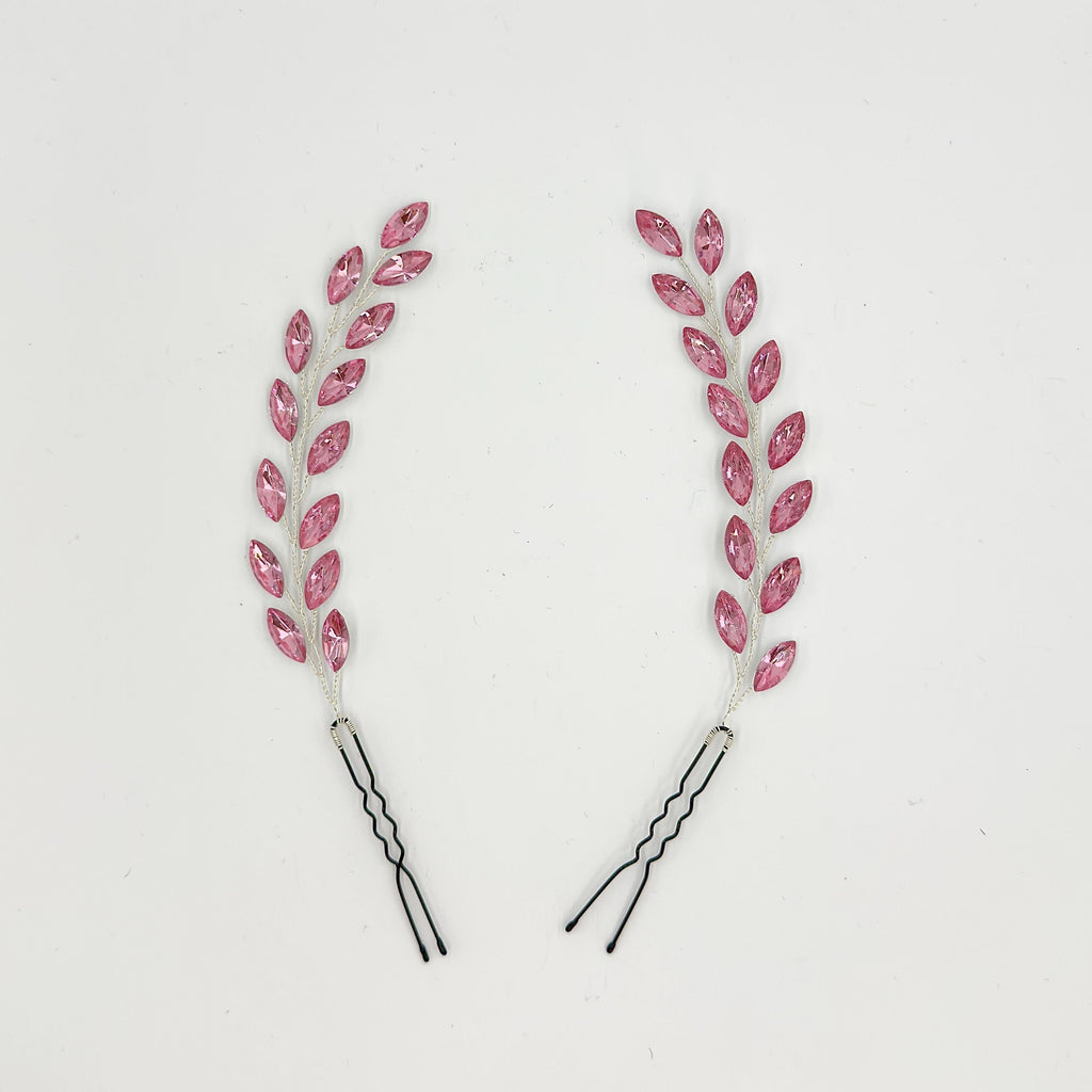 Two long bridal hair pins on a white background with pink leaf elements, silver-tone branches and black wavy pin bases.