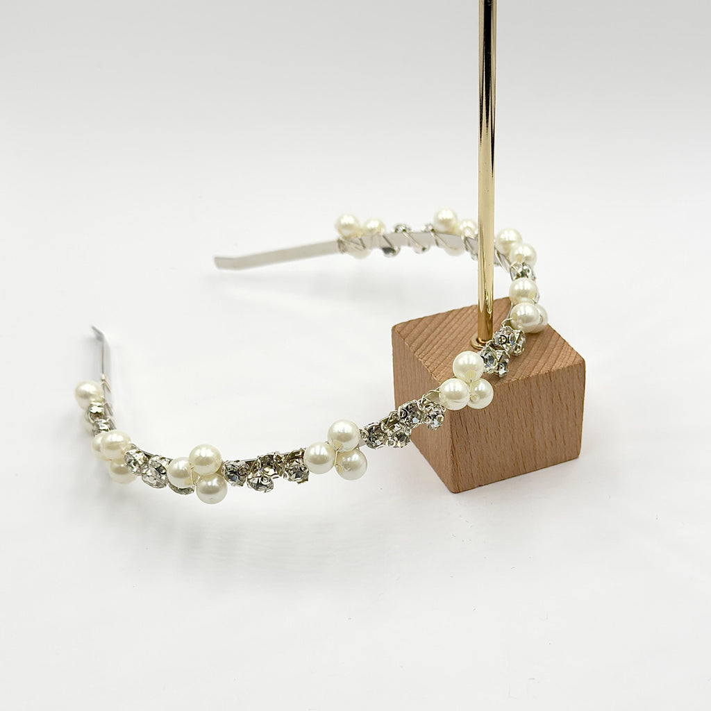 Blonde woman wearing a silver-tone bridal headband with white pearl clusters and clear round stones over loose, side-parted softly waved hair.