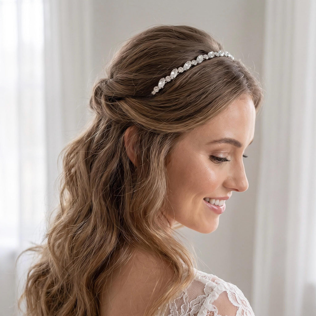 Bride wearing a silver-tone headband with clear round and elongated stones over side-parted hair styled in an elegant low bridal updo.