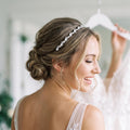 Braut trägt einen silberfarbenen Haarreif mit klaren runden und länglichen Steinen zu seitlich gescheiteltem Haar und einer eleganten tiefen Hochsteckfrisur.