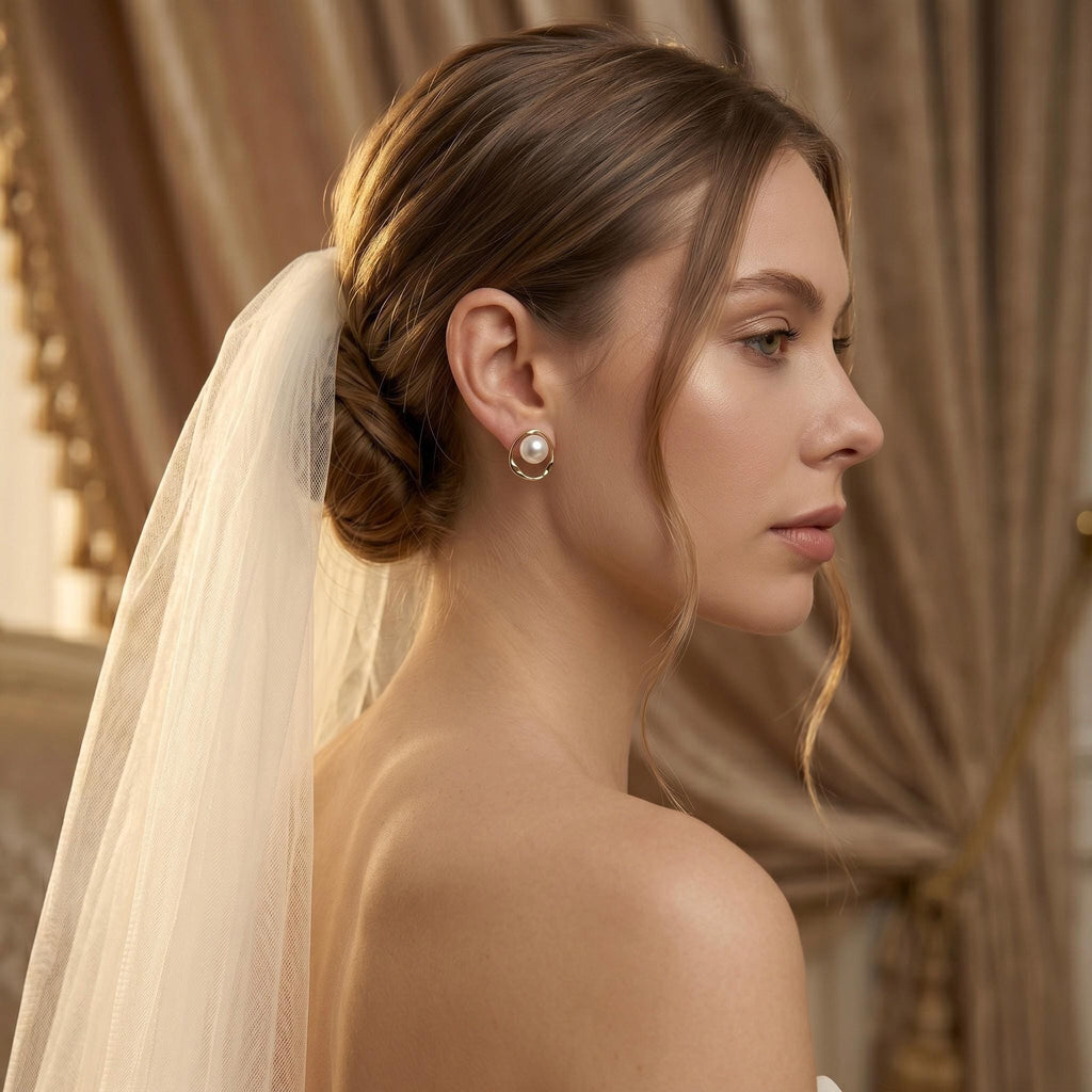 A woman in a white veil looks to the side, showcasing a gold-toned stud earring with a white pearl in a twisted open circle.
